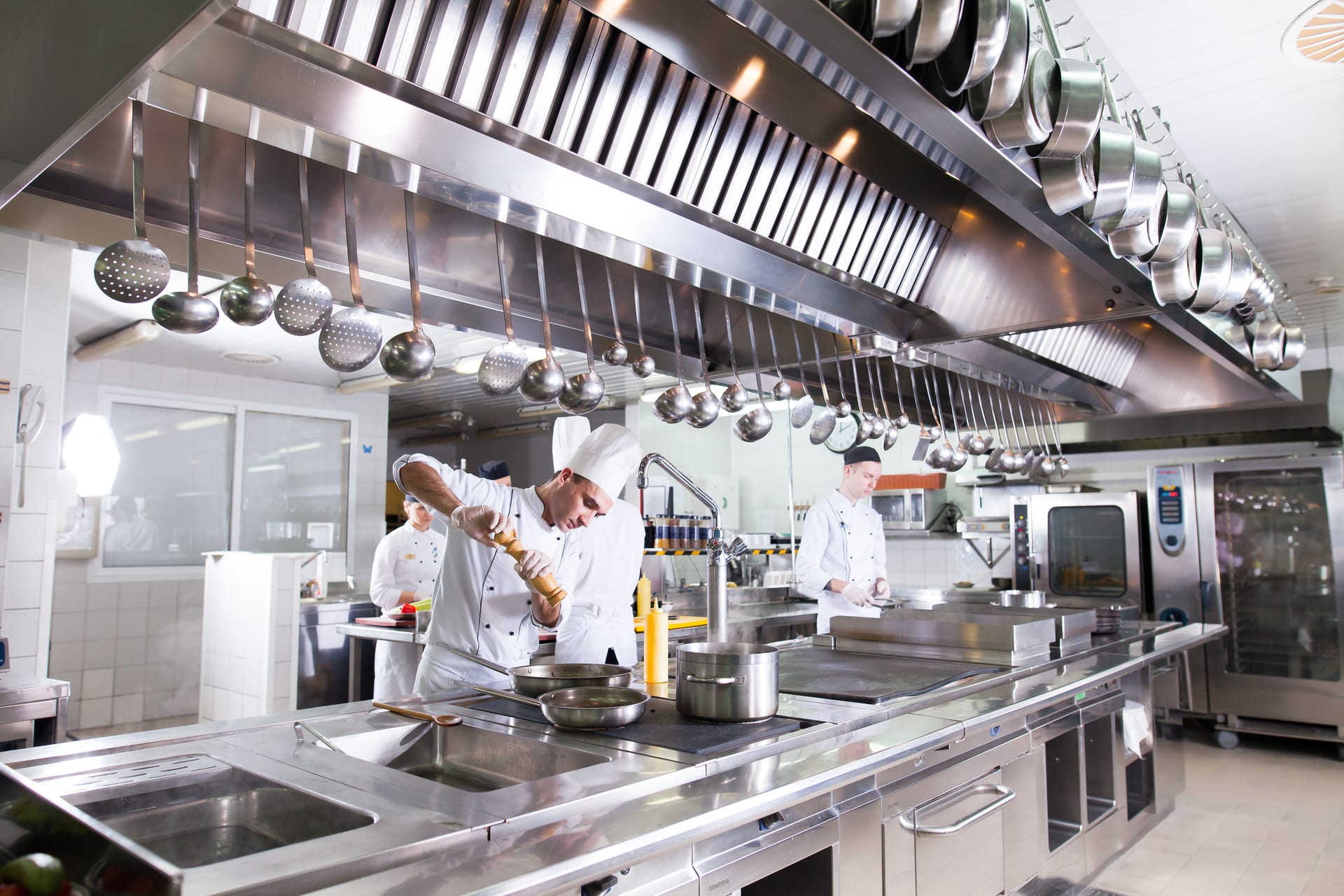 A chef seasons dishes in a professional commercial kitchen with connected appliances.